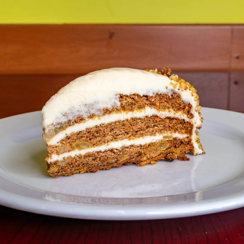 A slice of carrot cake with white cream cheese frosting and nuts on a white plate.